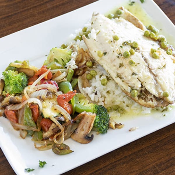 Villa Vinci's baked fish with rice, peas, and a side of sautéed vegetables on a white plate.