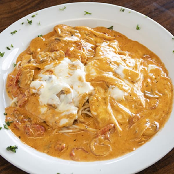 Creamy Italian pasta dish with chicken, mushrooms, and tomatoes, topped with melted cheese.