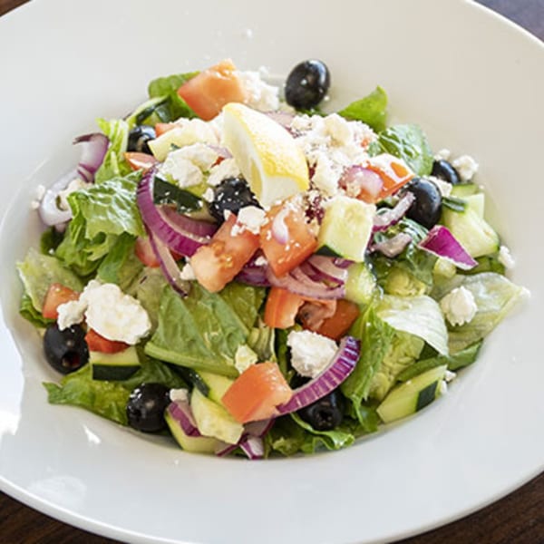 A fresh Villa Vinci Greek salad with lettuce, tomatoes, cucumbers, red onion, olives, feta, and lemon.