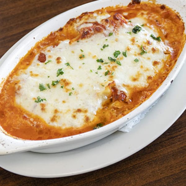 Baked Italian lasagna with melted cheese and parsley in a white oval dish on a wooden table.