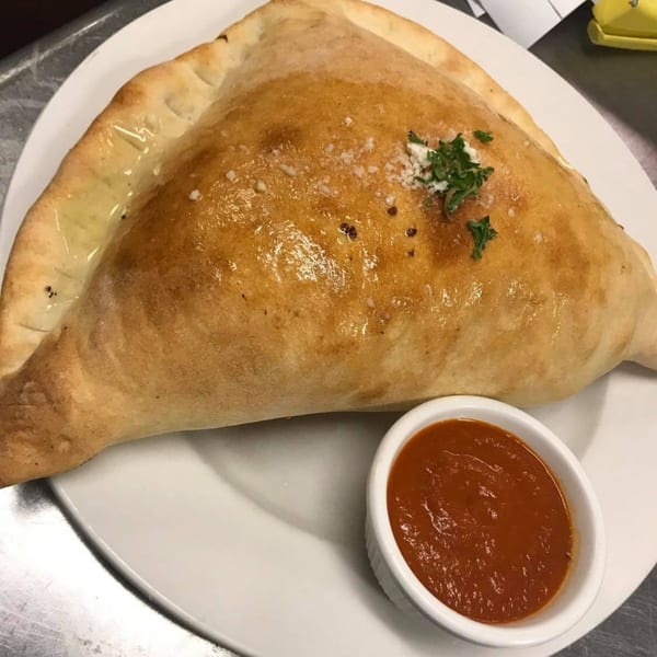 Golden-brown Villa Vinci calzone, sprinkled with cheese and parsley, served with a side of marinara sauce.