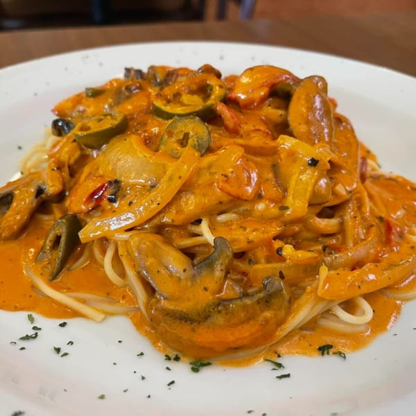 Creamy orange pasta with mushrooms, peppers, and olives on a white plate at Villa Vinci.