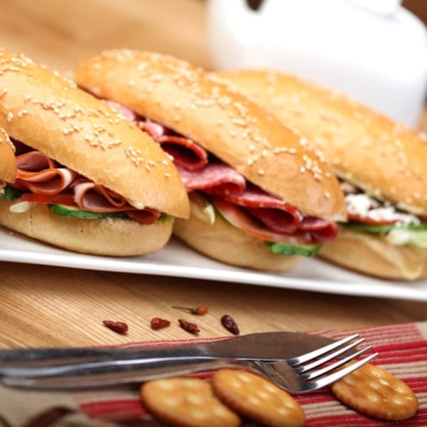 Three Italian subs with various meats and vegetables on a white platter, with crackers and cutlery.